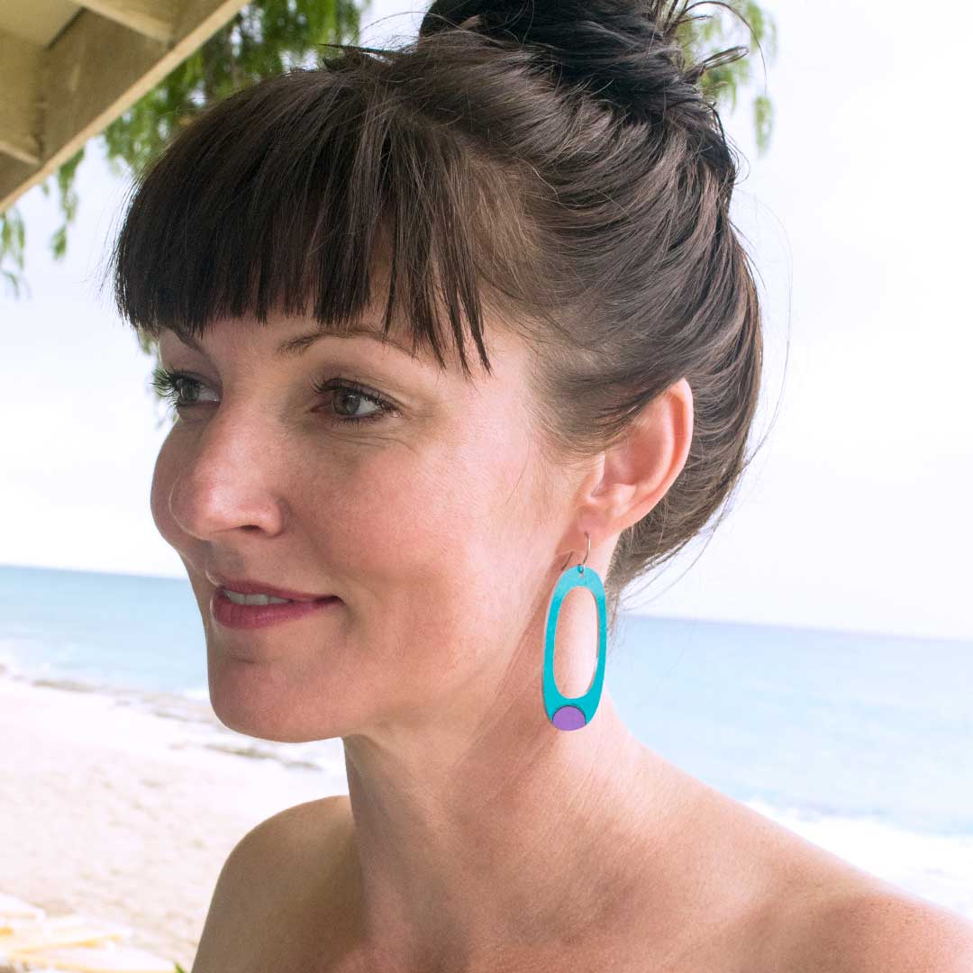 Adult woman wearing large hoop earrings in turquoise blue with mismatched purple and pink dots by ColorUpLife.