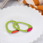 Large hoop earrings in bright green with mismatched orange and pink dots laying in a jewelry dish by ColorUpLife.