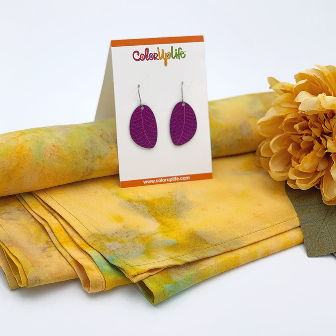 A pair of plum colored small leaf earrings displayed on a sunny yellow rayon scarf by ColorUpLife.