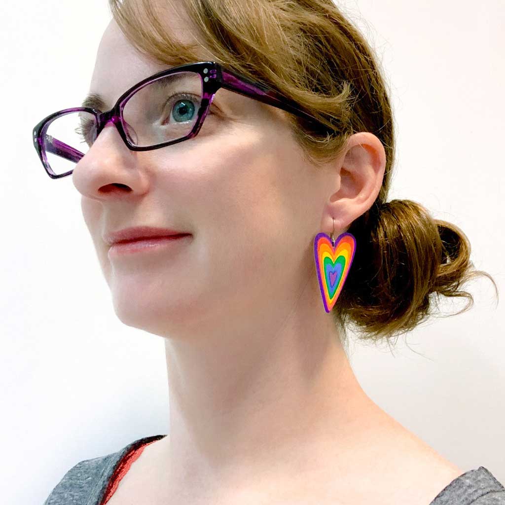 Young woman wearing rainbow heart dangle earrings by ColorUpLife.